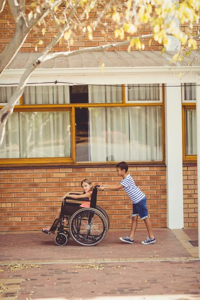 Scolaro spingendo ragazza su sedia a rotelle — Foto Stock
