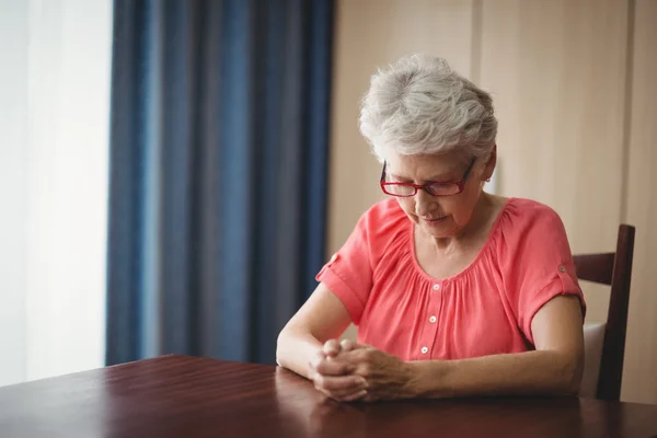 Задумчивая пожилая женщина сидит за столом — стоковое фото