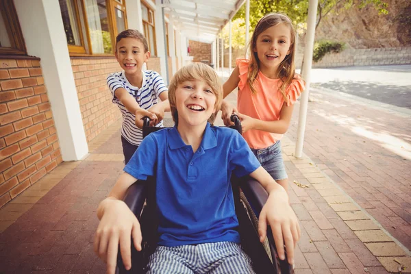 Les écoliers poussant garçon en fauteuil roulant — Photo