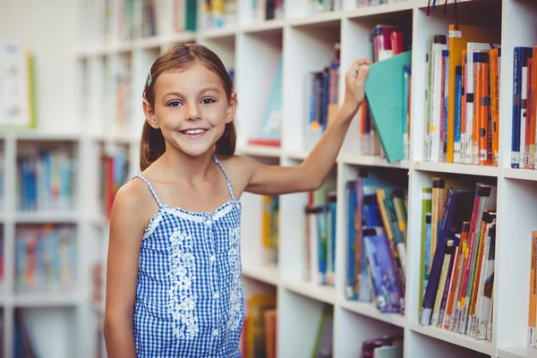 Chica de la escuela tomando un libro de la estantería — Foto de Stock