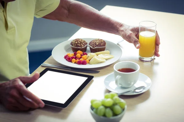 Hombre mayor usando tableta digital mientras desayuna — Foto de Stock