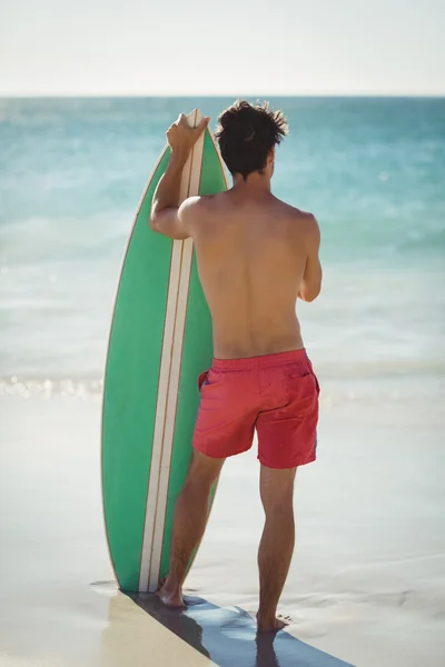 Mężczyzna stojący z deską surfingową na plaży — Zdjęcie stockowe