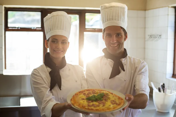 Två kocken presenterar en pizza — Stockfoto