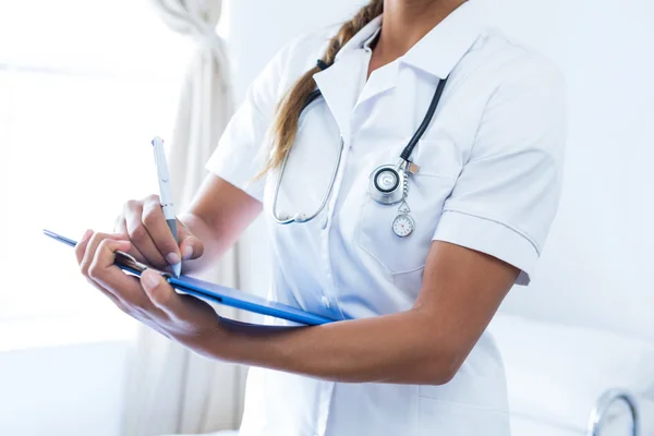 Female doctor writing on clipboard in hospital — Stock Photo, Image