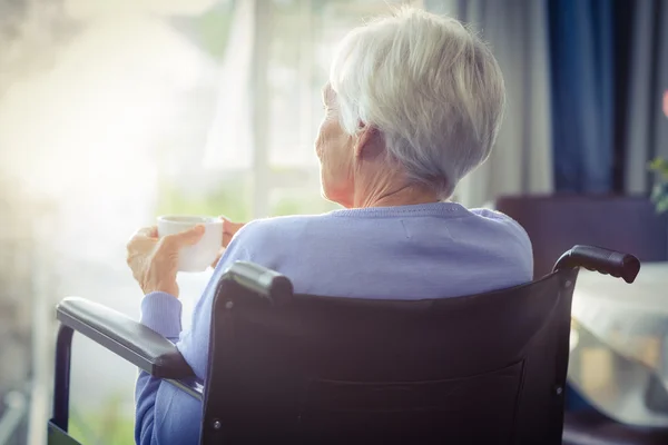 Vista posteriore della donna anziana sulla sedia a rotelle che tiene una tazza di tè — Foto Stock