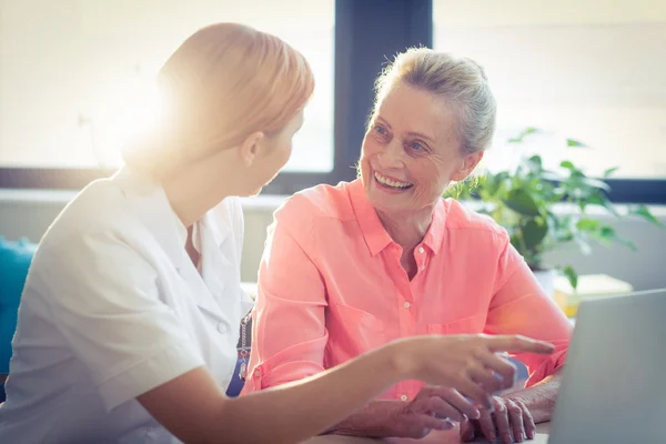 Kobiece pielęgniarka i starszy kobieta uśmiechając się podczas korzystania z laptopa — Zdjęcie stockowe