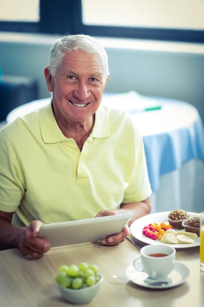 Senior man met behulp van digitale tablet tijdens het ontbijt — Stockfoto