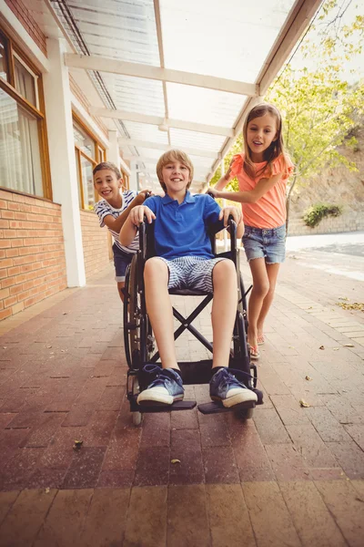 Les écoliers poussant garçon en fauteuil roulant — Photo