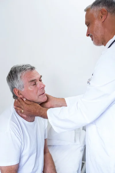 Male doctor examining senior mans neck — Stock Photo, Image