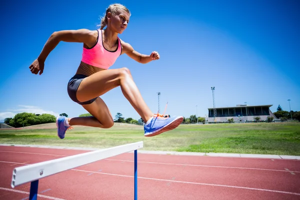 Female athlete jumping above the hurdle — Stock Photo, Image