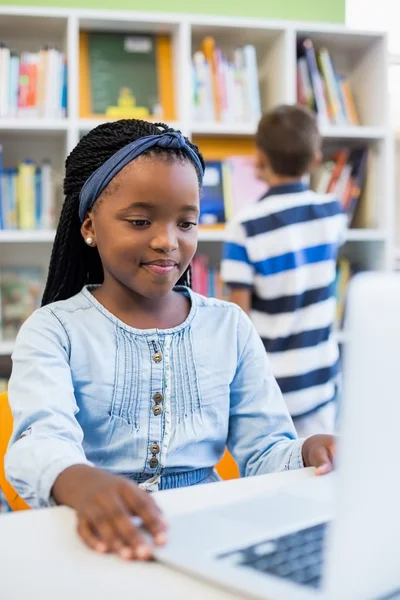 Skolflicka med laptop i biblioteket — Stockfoto