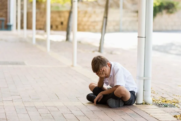 Sad schoolboy sitting alone in corridor — Stock Photo, Image