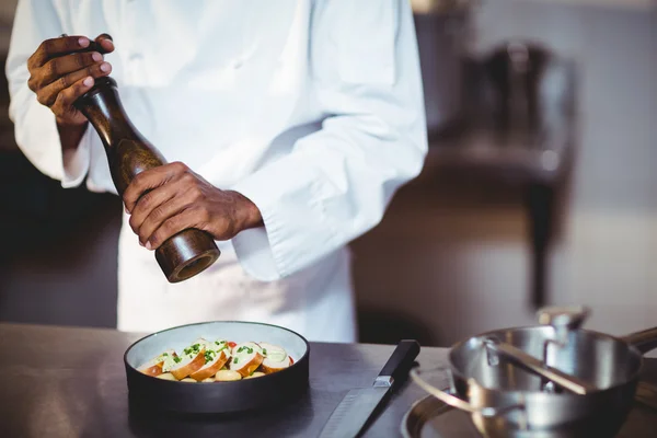 Chef sprinkling pepper on a meal — Stock Photo, Image