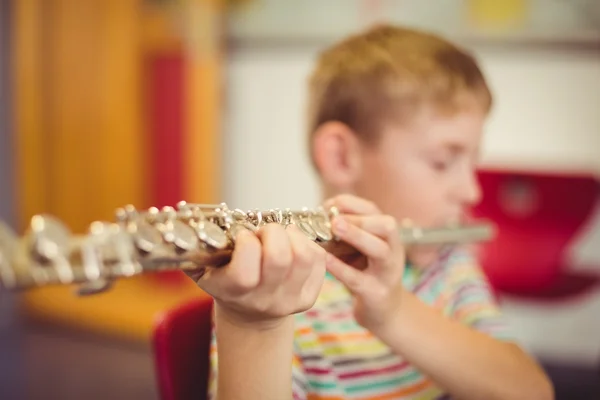 Schoolboy playing flute in classroom — Stock Photo, Image