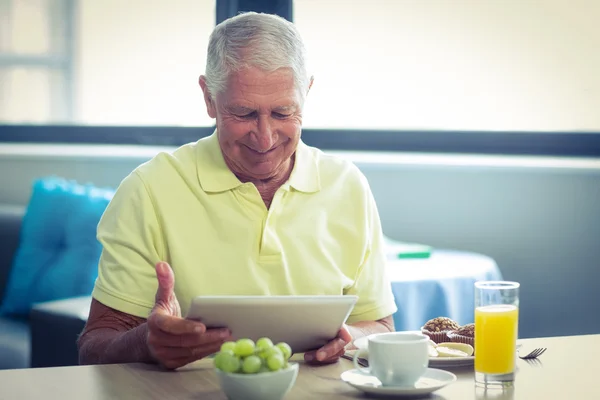 Homem sênior usando tablet digital enquanto toma café da manhã — Fotografia de Stock