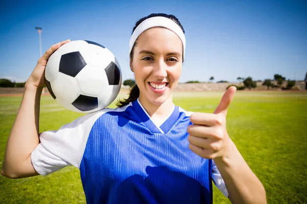 Jugadora de fútbol feliz sosteniendo una pelota y mostrando sus pulgares hacia arriba — Foto de Stock