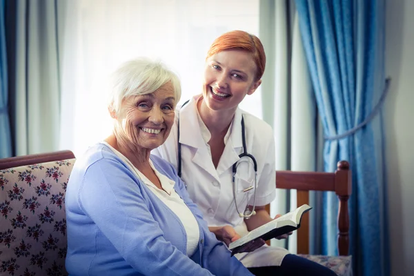 Médico sonriente ayudando a una mujer mayor a leer un libro —  Fotos de Stock