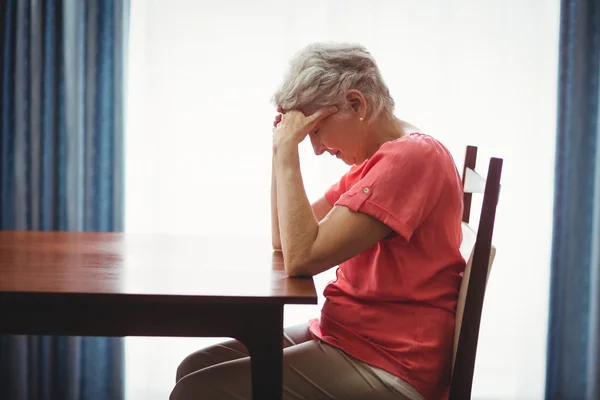 Smutný starší žena sedí u stolu — Stock fotografie