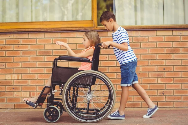 Schoolboy pushing a girl on wheelchair — Stock Photo, Image