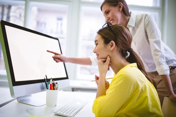 businesswoman pointing at computer to colleague