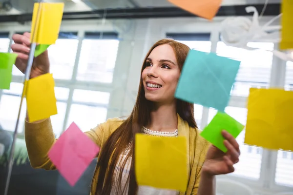 Empresária anexando notas pegajosas em vidro — Fotografia de Stock