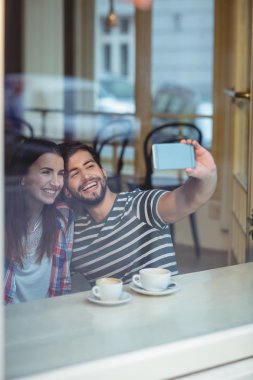 Cheerful couple taking selfie at cafe clipart