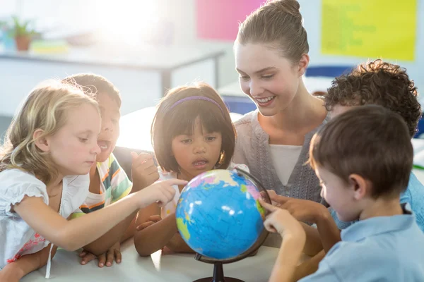 Teacher looking at schoolchildren touching globe — Stock Photo, Image