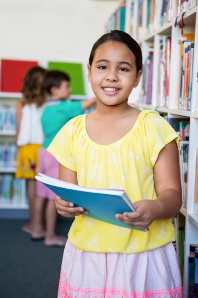 Niña de primaria sosteniendo libros en la biblioteca escolar — Foto de Stock