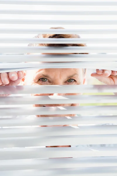 Rijpe vrouw op zoek via blinds — Stockfoto