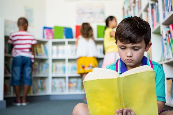 Menino elementar lendo livro na biblioteca da escola — Fotografia de Stock