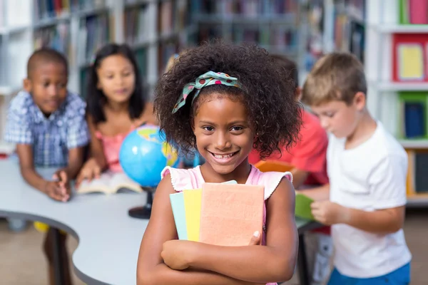 Menina feliz segurando livros contra colegas de classe — Fotografia de Stock
