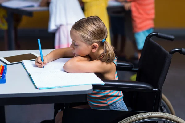 Chica en silla de ruedas escribiendo en libro —  Fotos de Stock