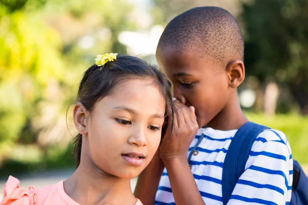 Schoolboy whispering to girl at campus — Stock Photo, Image