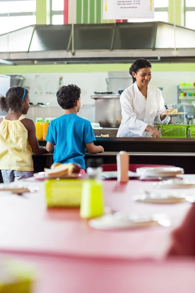 Mulher servindo comida para crianças em idade escolar — Fotografia de Stock