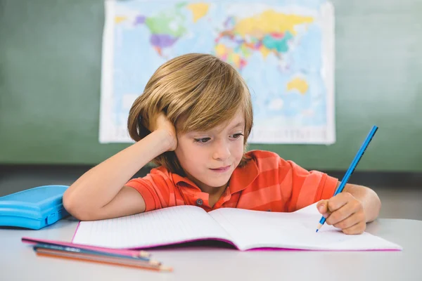 Boy writing on book in classroom — Stock Photo, Image