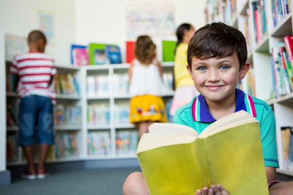 Niño sosteniendo libro en la biblioteca escolar — Foto de Stock