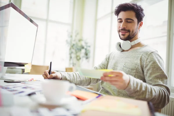 Businessman writing from note in office — Stock Photo, Image