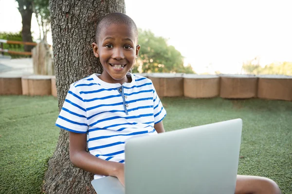 Šťastný chlapec pomocí přenosného počítače v parku — Stock fotografie