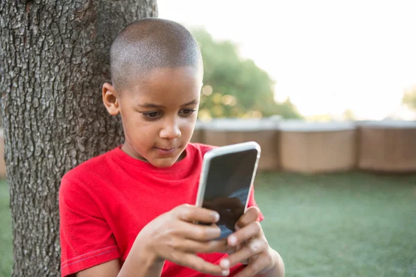 Elementary boy using phone at park — Stock Photo, Image