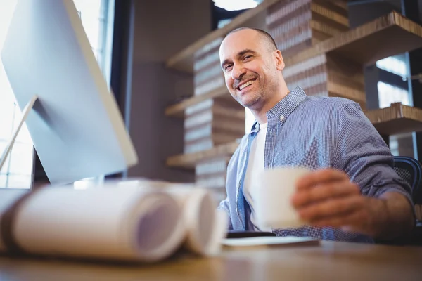 Businessman holding cup at computer desk — Stock Photo, Image