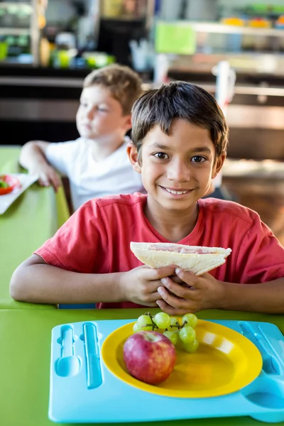 Счастливый мальчик с одноклассниками обедает — стоковое фото