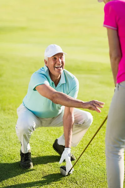 Golfer man crouching while teaching woman — Stock Photo, Image
