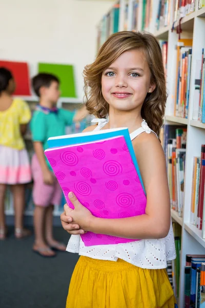 Linda chica sosteniendo libros en la biblioteca de la escuela —  Fotos de Stock