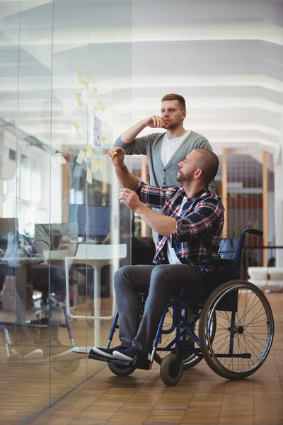 Инвалидный бизнесмен и его коллега приклеивают заметки — стоковое фото