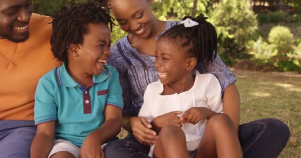 Семья сидит в траве и смеется — стоковое видео