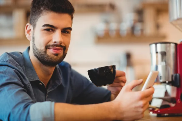 Joven sosteniendo teléfono móvil y taza de café —  Fotos de Stock