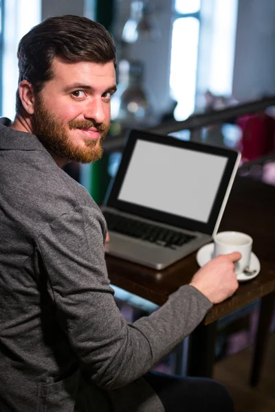 Homem segurando xícara de café e usando laptop — Fotografia de Stock