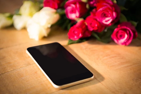 Rosas amarillas y rojas con smartphone en la mesa de madera —  Fotos de Stock