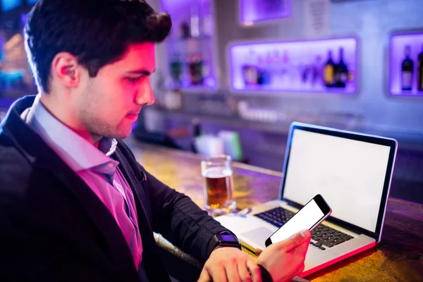 与玻璃的啤酒和桌子上的手提电脑使用手机的人 — 图库照片