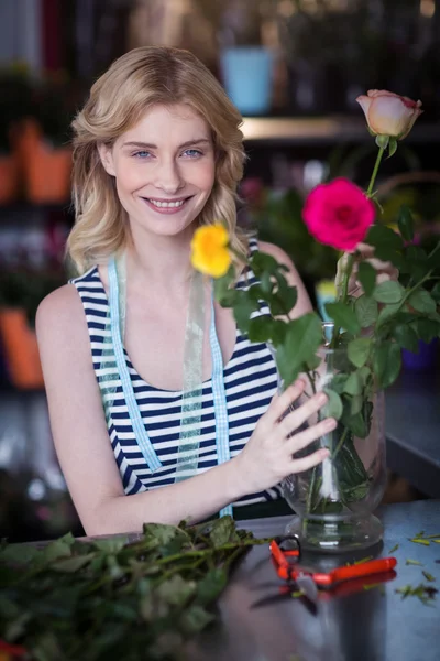 Glimlachend vrouwelijke bloemist inrichtend bloemboeket in vaas op flowe — Stockfoto